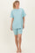 woman wearing a light blue oversized t-shirt and matching bike shorts, standing barefoot on a neutral background