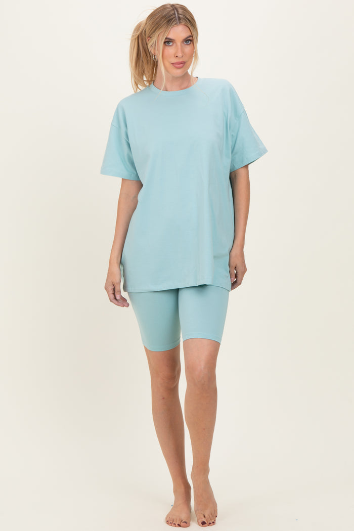 woman wearing a light blue oversized t-shirt and matching bike shorts, standing barefoot on a neutral background