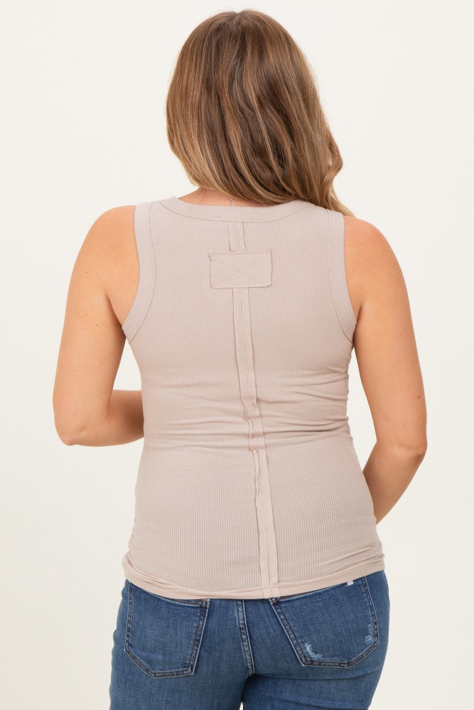 woman wearing a beige maternity tank top with a back button detail and paired with blue jeans.