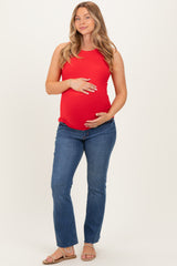 woman wearing a red maternity tank top and blue jeans, showing her baby bump while smiling