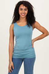 woman wearing a light blue form-fitting tank top and blue high-waisted jeans, smiling at the camera
