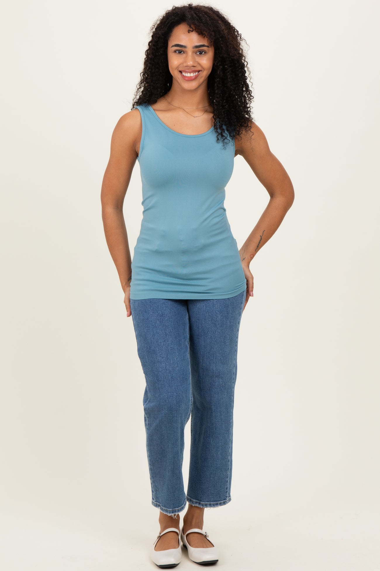 woman wearing a light blue fitted tank top and high-waisted straight leg jeans with white slip-on shoes