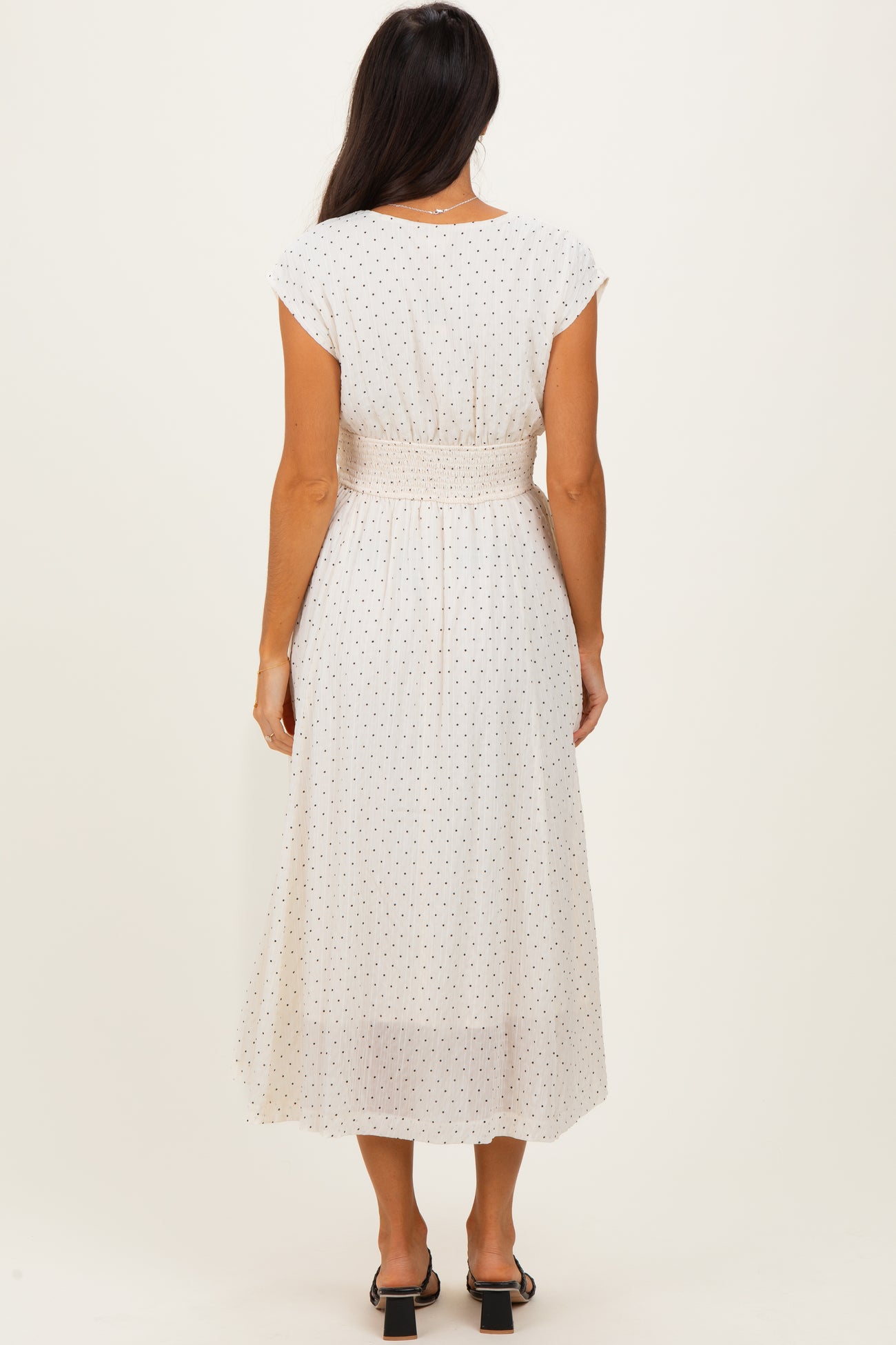 woman wearing a white midi dress with polka dots and a smocked waist, viewed from the back