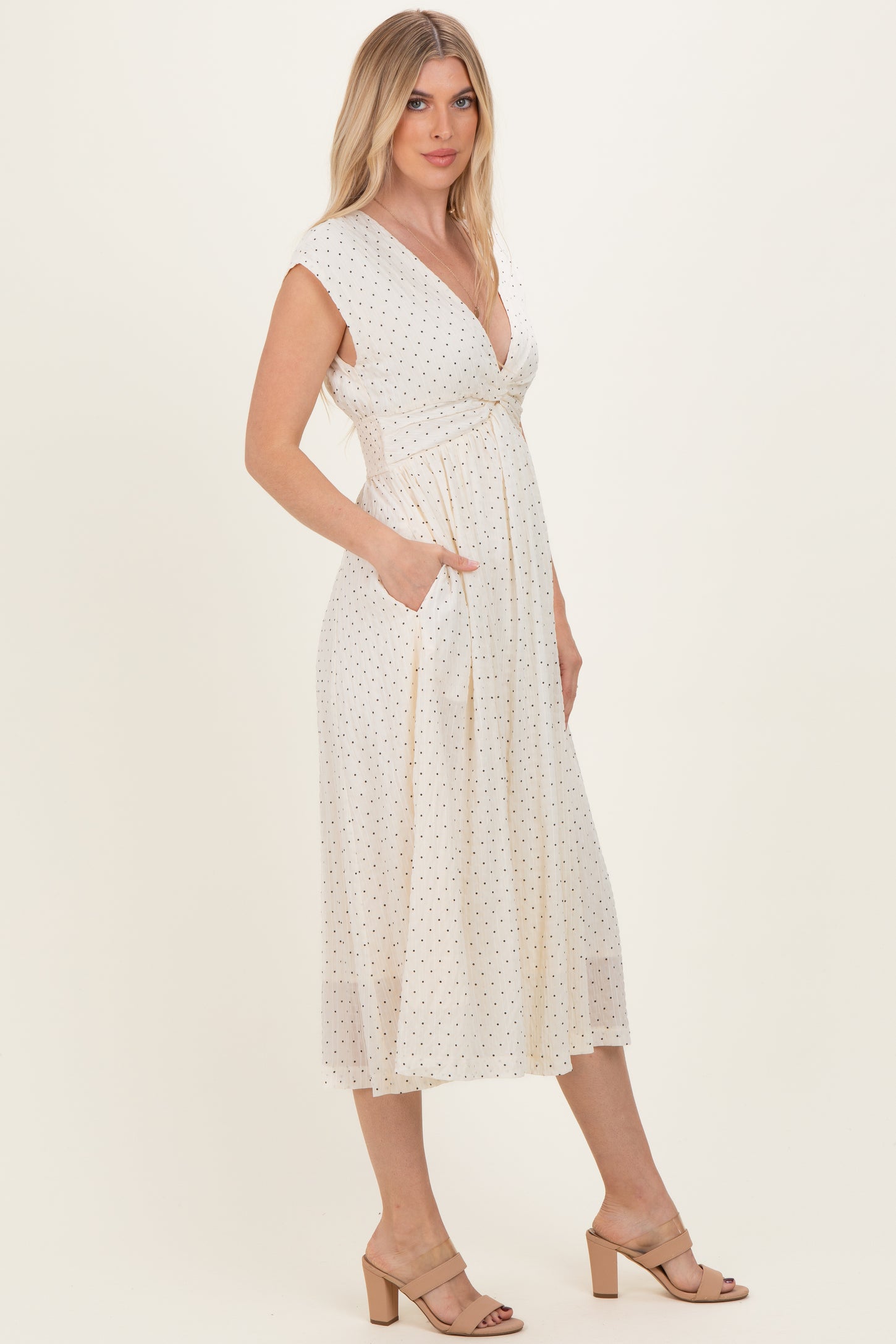 woman wearing a cream polka dot midi dress with a deep v-neck and pockets, paired with tan block heel sandals