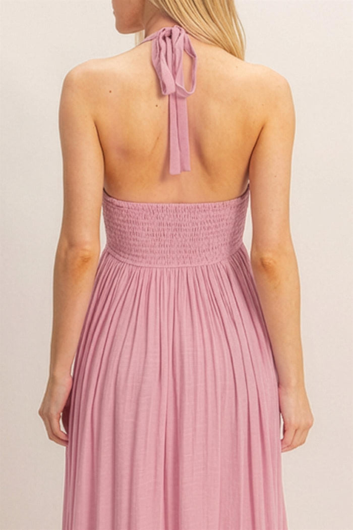 woman wearing a back view of a light pink halter neck maxi dress with a smocked bodice