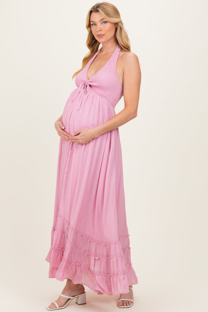 woman wearing a light pink halter neck maternity maxi dress holding her baby bump
