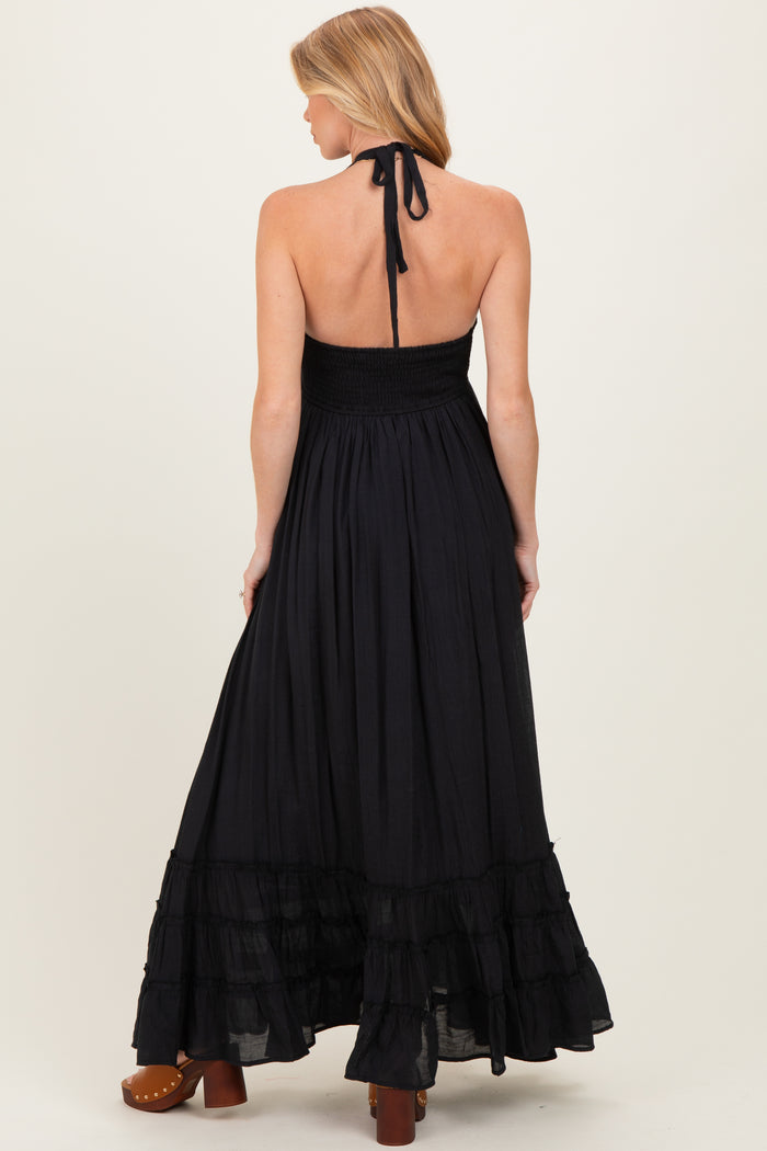 woman wearing a black halter neck maternity maxi dress with a smocked bodice and tiered ruffle hem