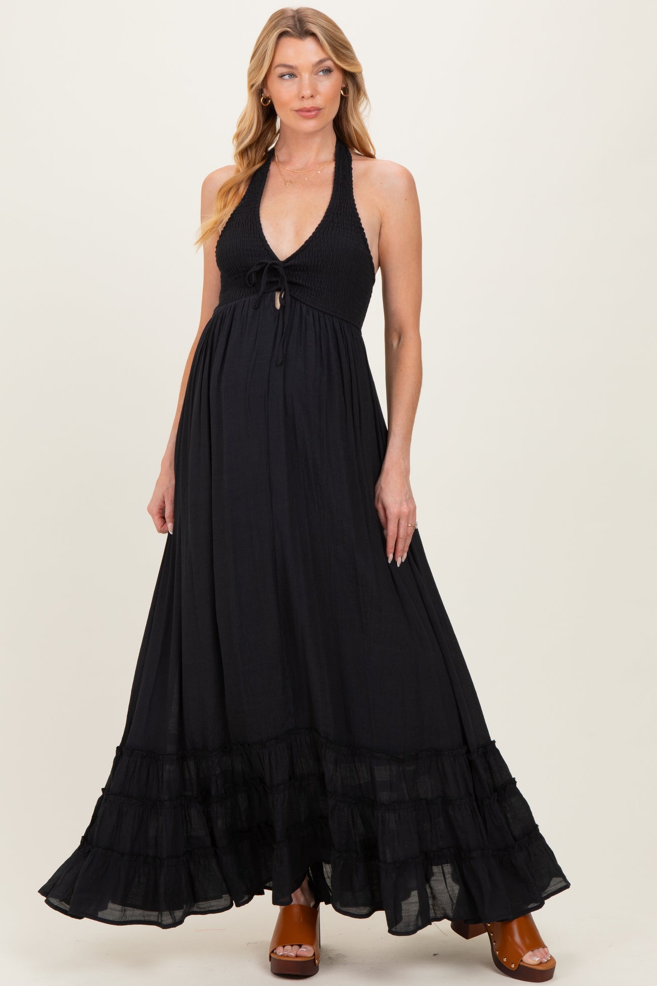 woman wearing a black halter maternity maxi dress with a smocked bodice and ruffled hem, showcasing her baby bump