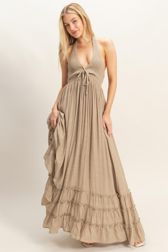 woman wearing a tan halter neck maxi dress with a tie front and ruffled hemline