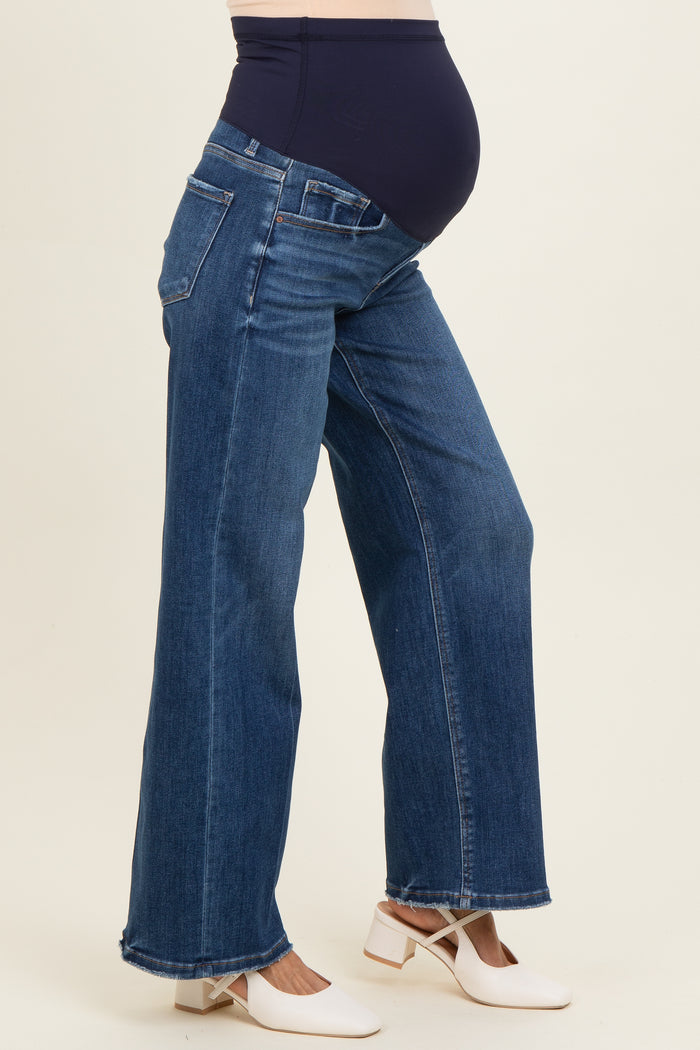 woman wearing blue maternity jeans with a stretchy waistband, showing a visible baby bump and white block-heeled shoes