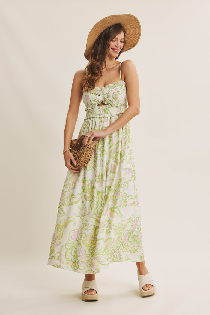 woman wearing a floral print maxi dress with spaghetti straps and a straw hat, holding a woven bag