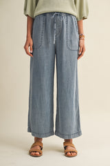 woman wearing light blue wide-leg denim pants with elastic waistband and side pockets, styled with casual sandals