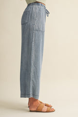 woman wearing light blue wide leg denim pants with an elastic waistband and side pockets, styled with brown sandals
