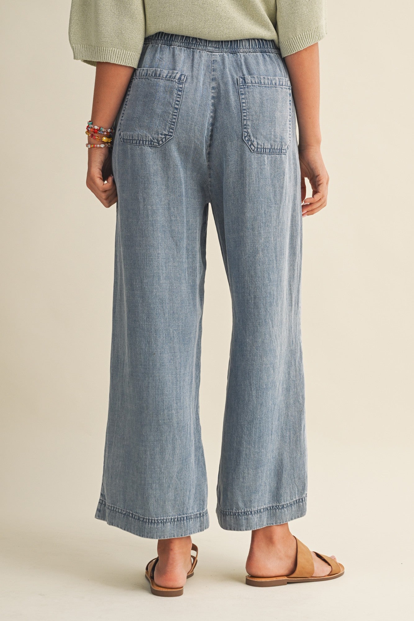 woman wearing light blue wide-leg chambray pants with an elastic waistband, showing the back view and two back pockets