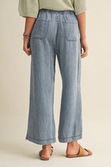 woman wearing light blue wide-leg chambray pants with an elastic waistband, showing the back view and two back pockets