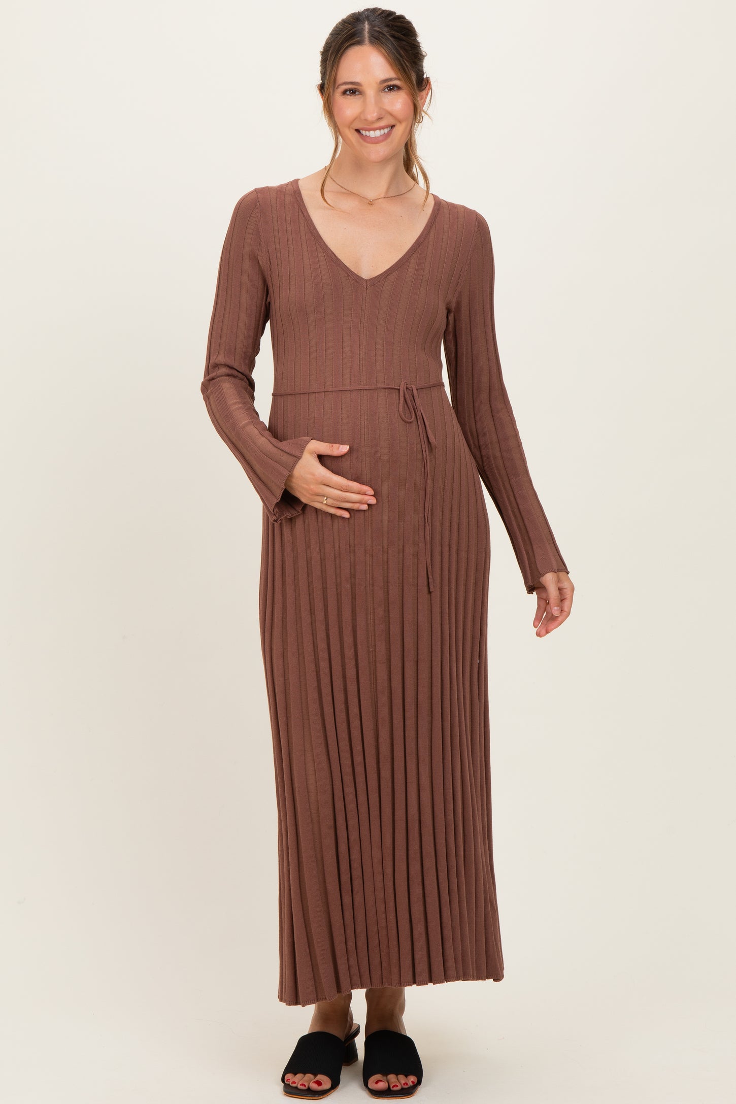 woman wearing a brown ribbed maternity maxi dress with a tie waist and holding her baby bump