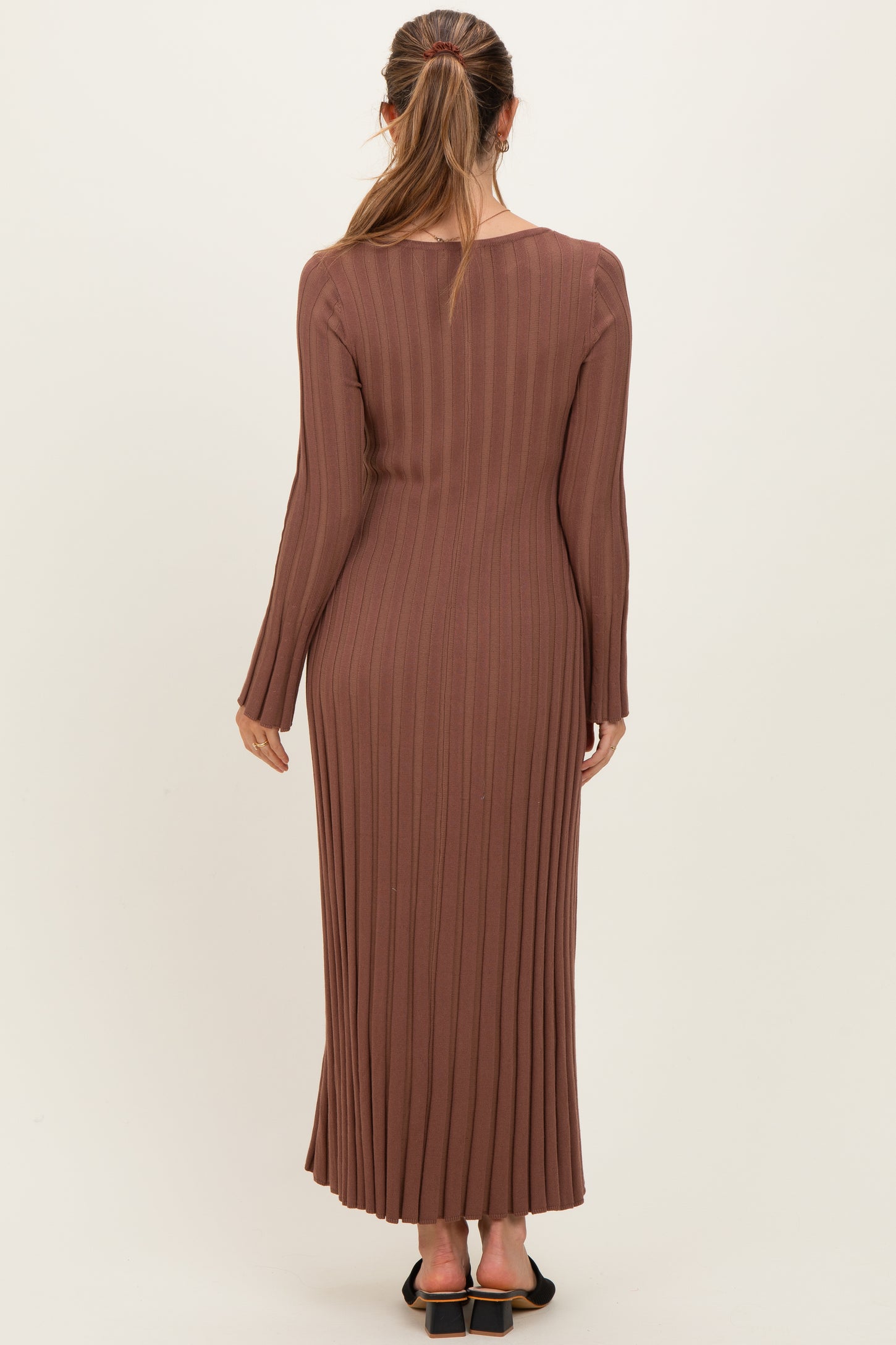 woman wearing a brown ribbed maternity maxi dress with long sleeves, showing a fitted silhouette from the back