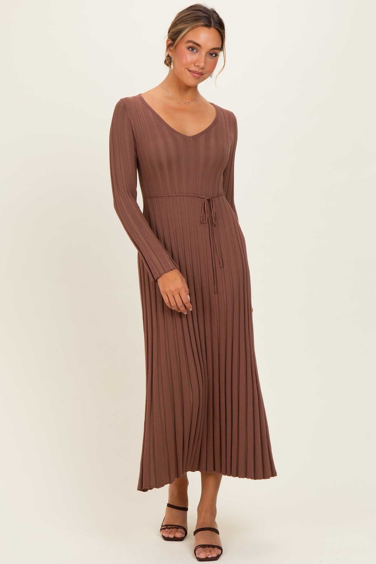 woman wearing a brown long sleeve pleated maxi dress with a drawstring waist and strappy black heels