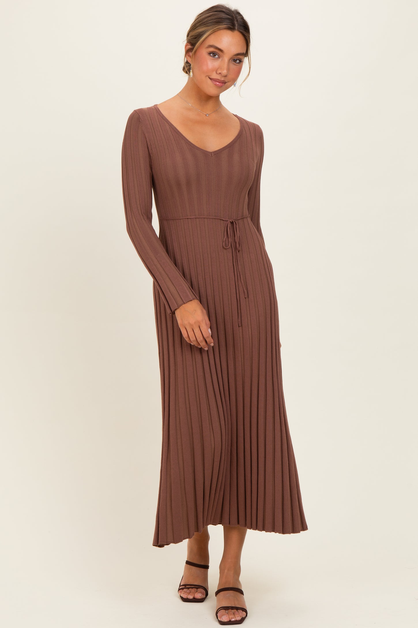 woman wearing a brown long sleeve pleated maxi dress with a drawstring waist and strappy black heels
