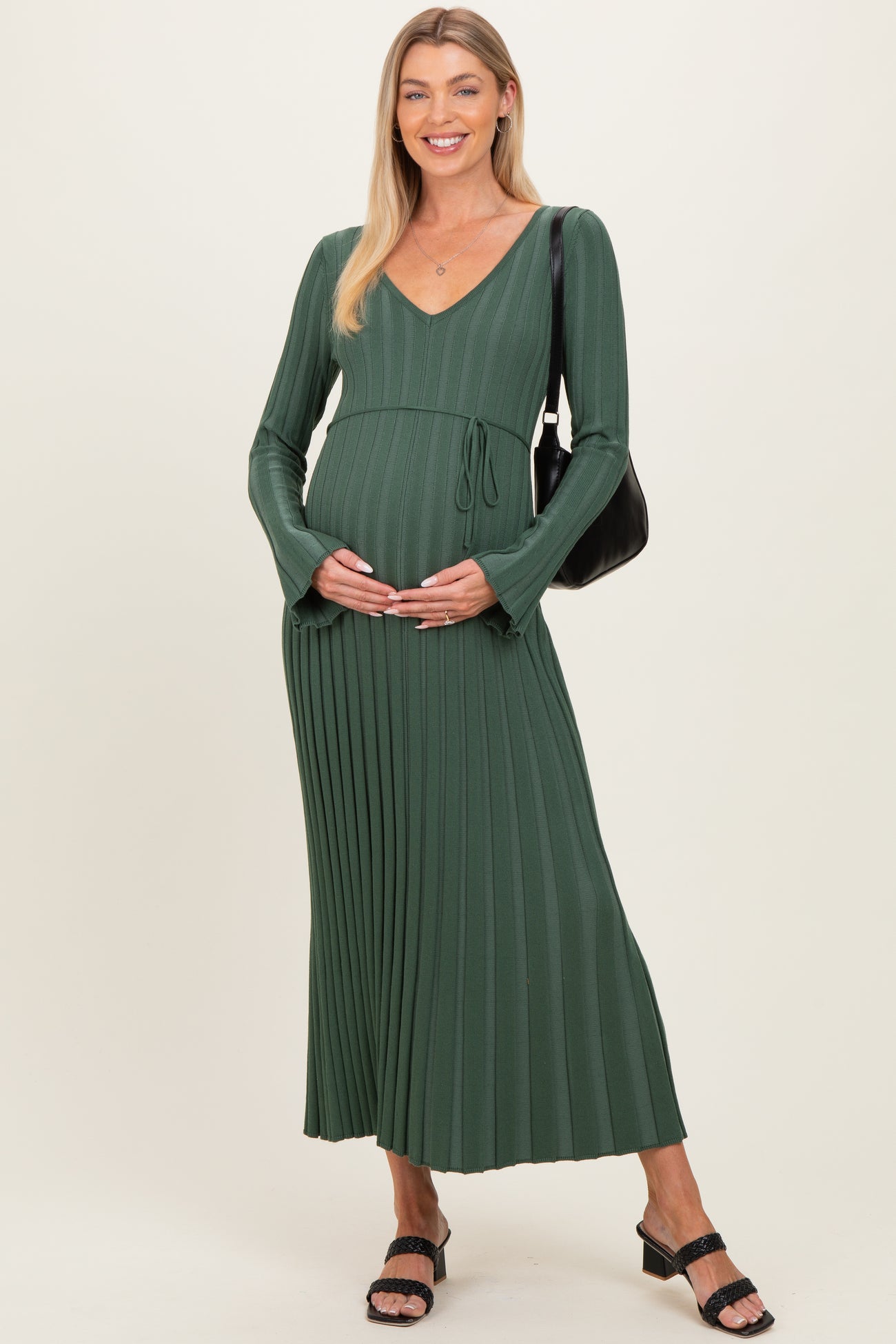 woman wearing a green long sleeve maternity dress with pleats, holding her baby bump