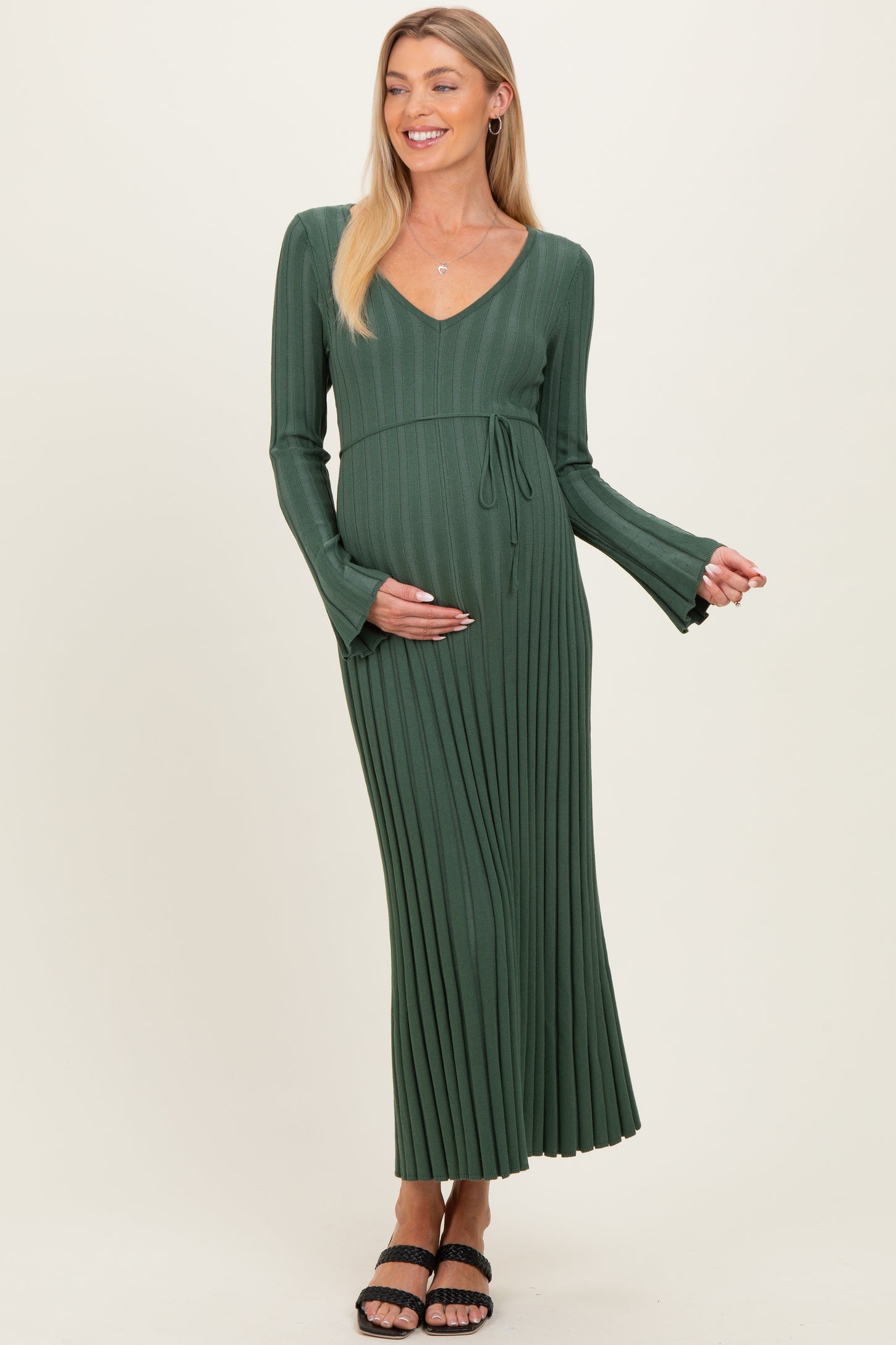 woman wearing a green pleated maternity dress with a v-neck and long sleeves, showing her baby bump