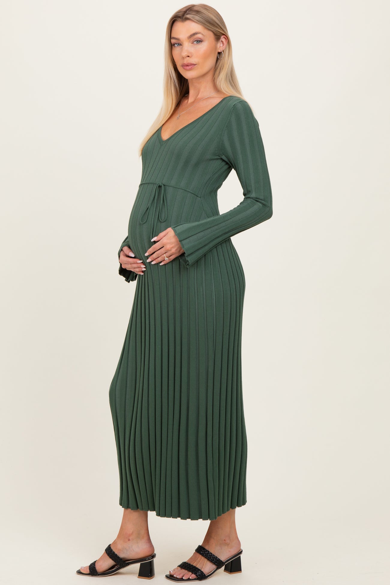 woman wearing a dark green ribbed maternity dress with a tie waist and a visible baby bump