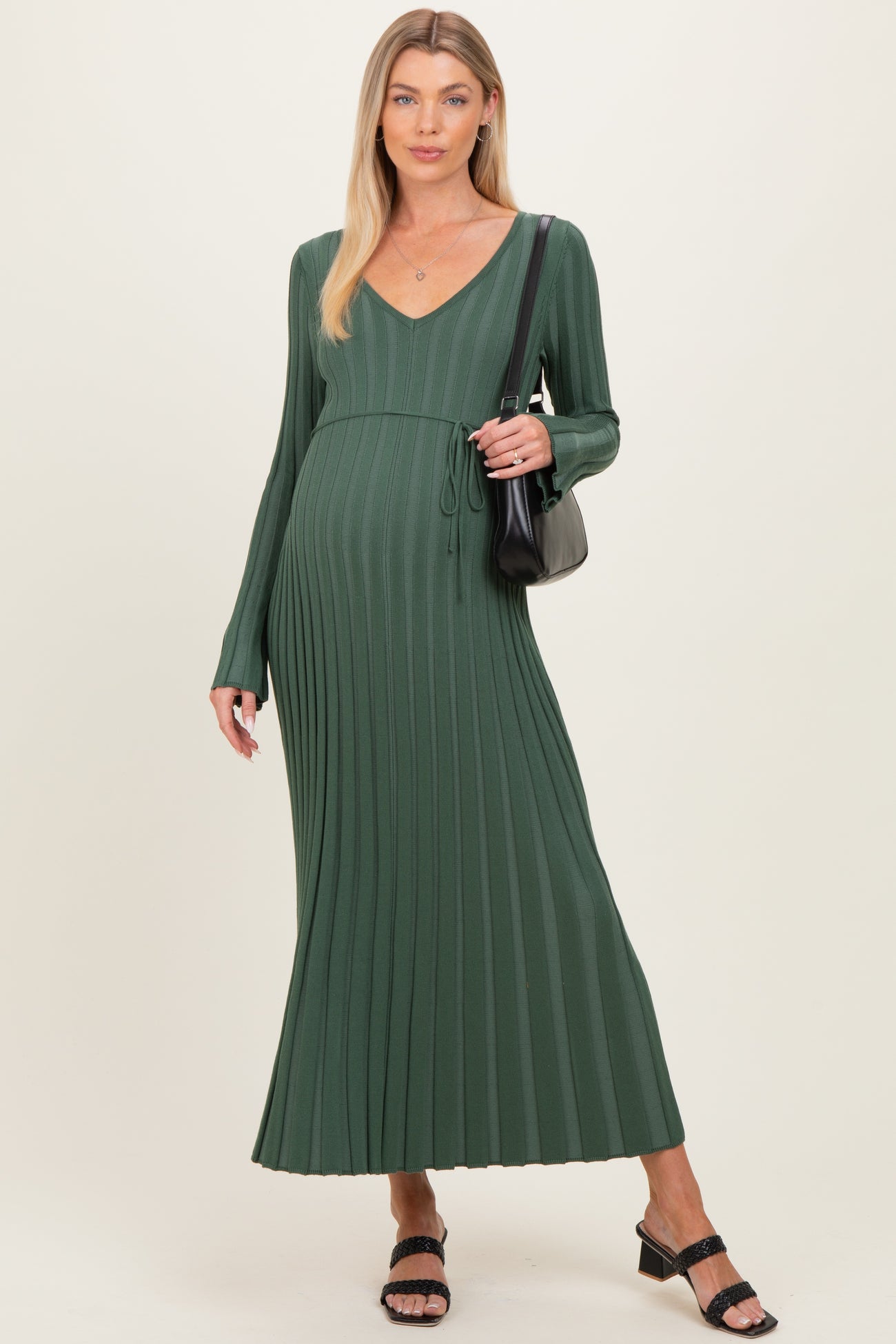 woman wearing a dark green maternity maxi dress with ribbed detailing and a tie waist, carrying a black handbag