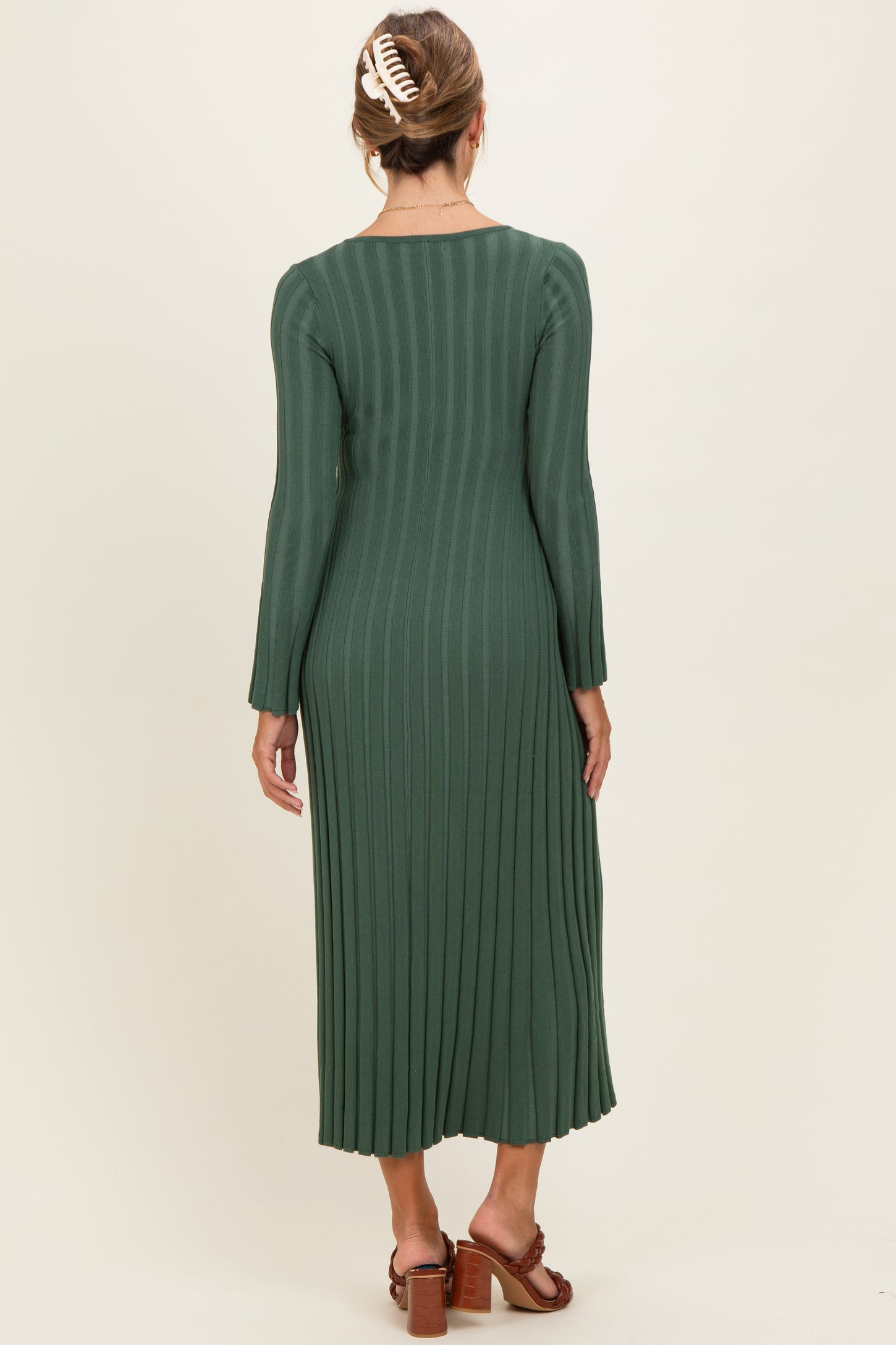 woman wearing a dark green long sleeve ribbed midi dress with a back view showing pleats and a flowy silhouette