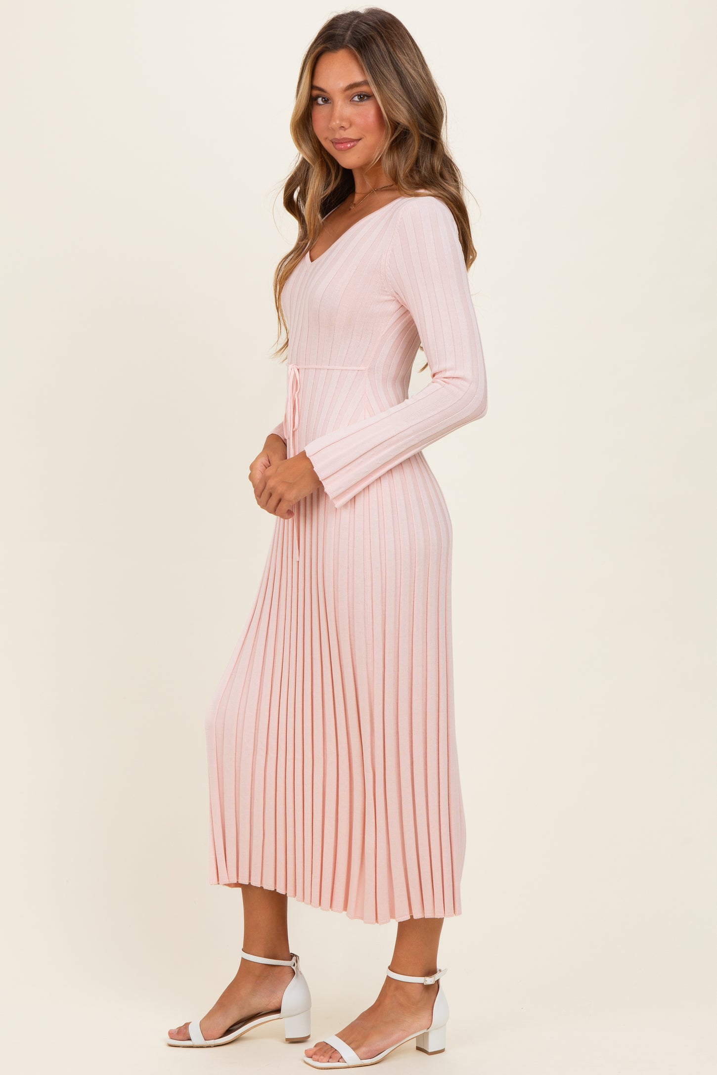 woman wearing a light pink ribbed midi dress with long sleeves and a tie waist detail