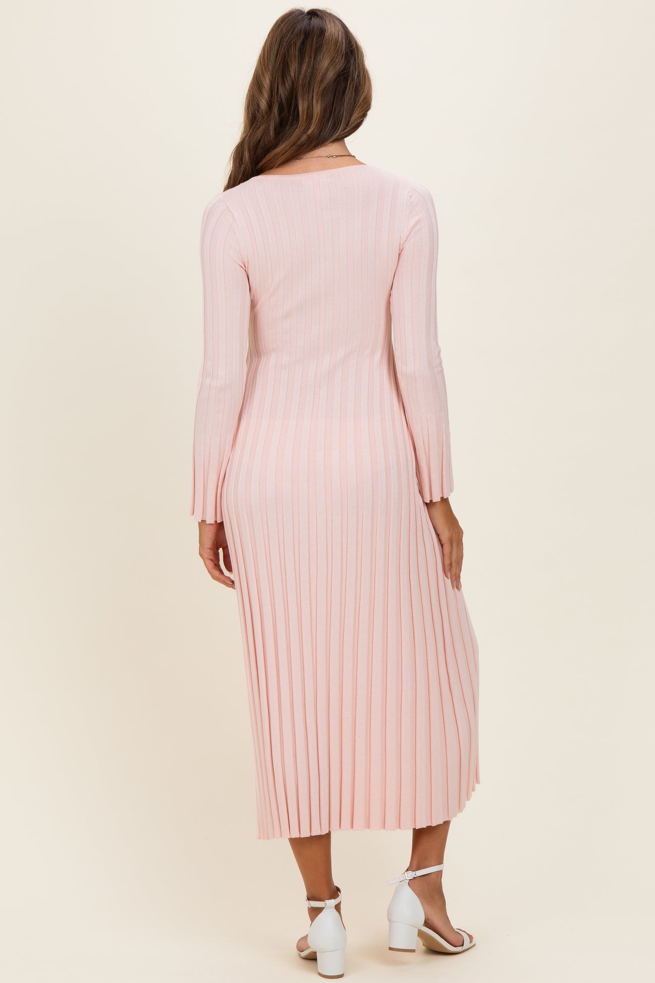 woman wearing a light pink pleated maxi dress with long sleeves, showing the back view