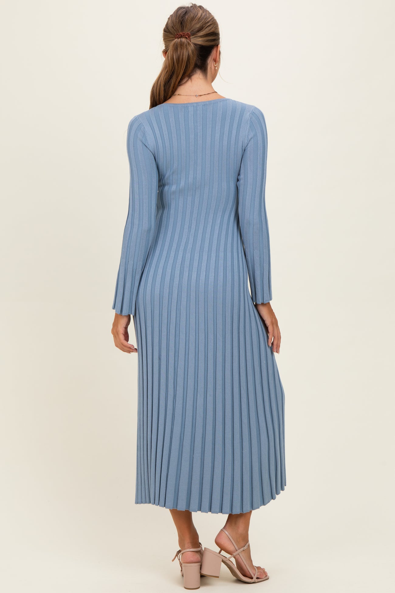 woman wearing a long sleeve ribbed midi dress in light blue, showing the back view with a fitted silhouette and side pleats