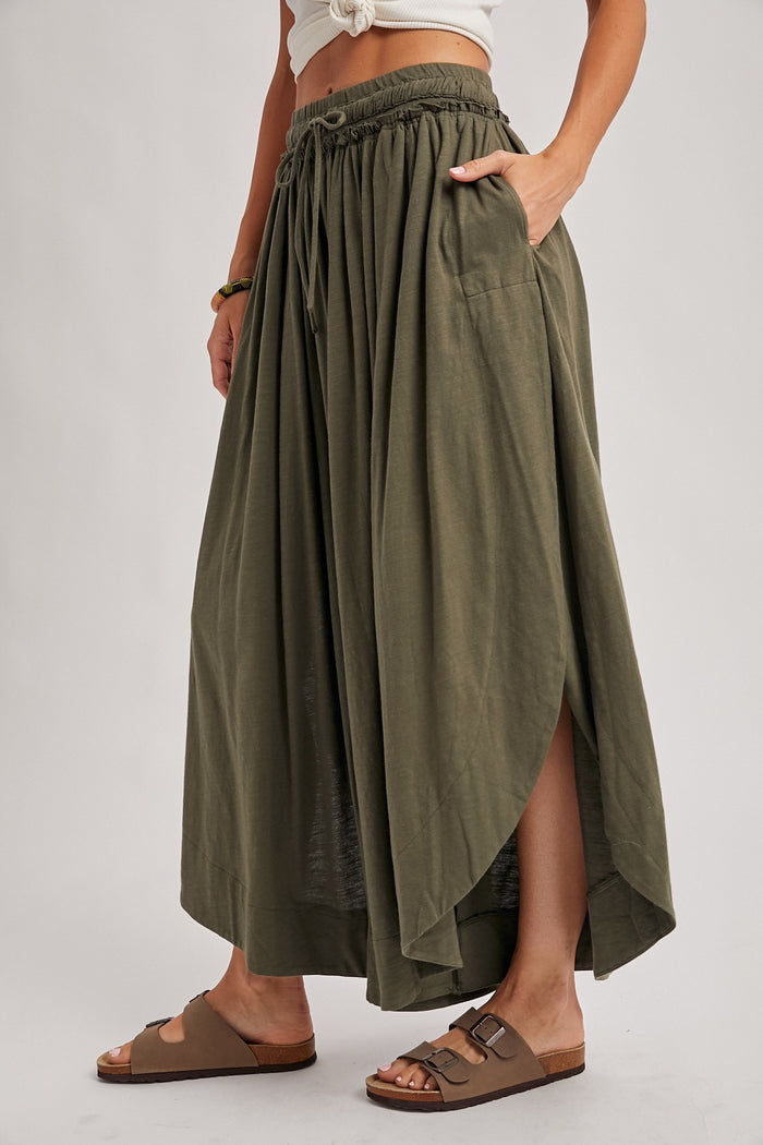 woman wearing an olive green maxi skirt with a high slit and side pockets