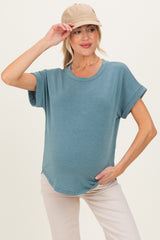 woman wearing a blue short sleeve maternity top with a relaxed fit and holding a beige cap, showing her baby bump