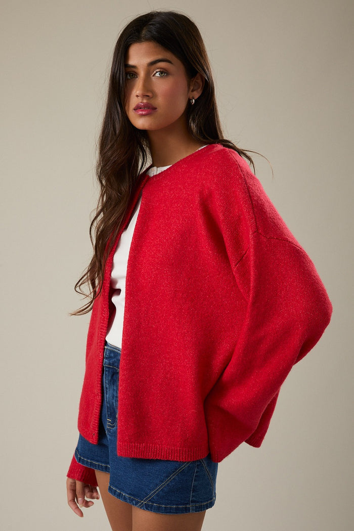 woman wearing a red oversized cardigan over a white top and denim shorts