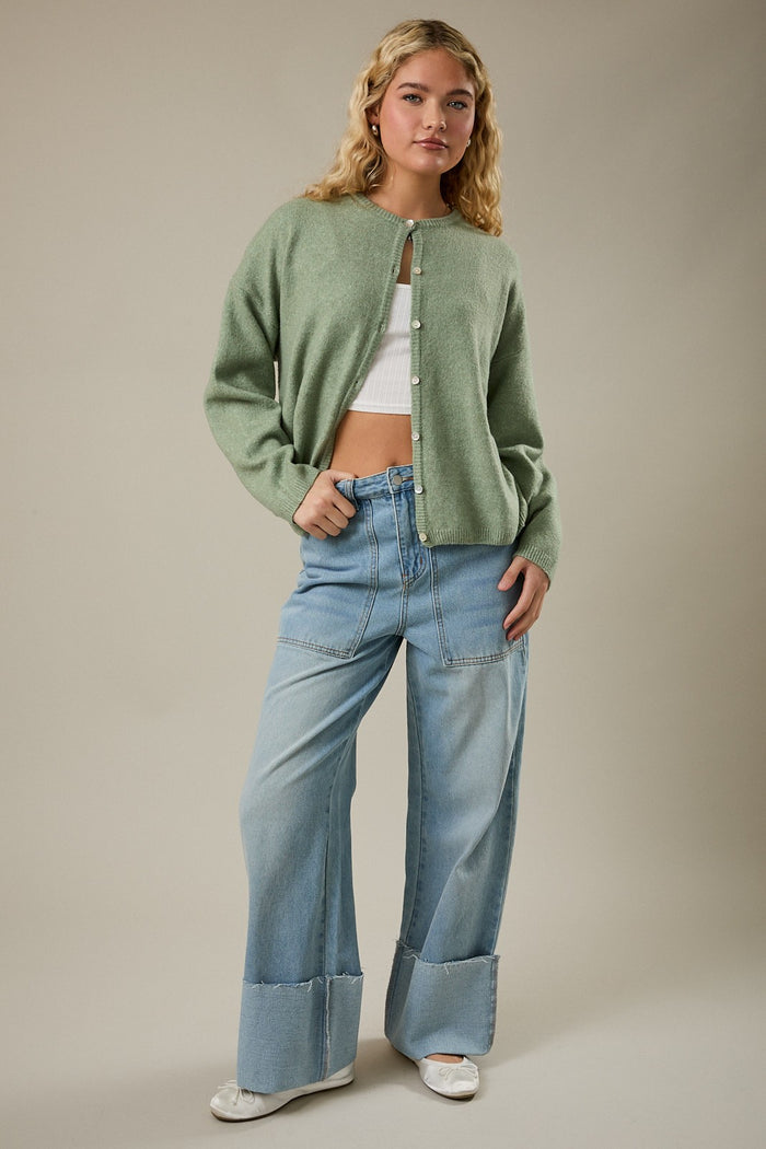 woman wearing a green cardigan over a white crop top and light blue wide-leg jeans