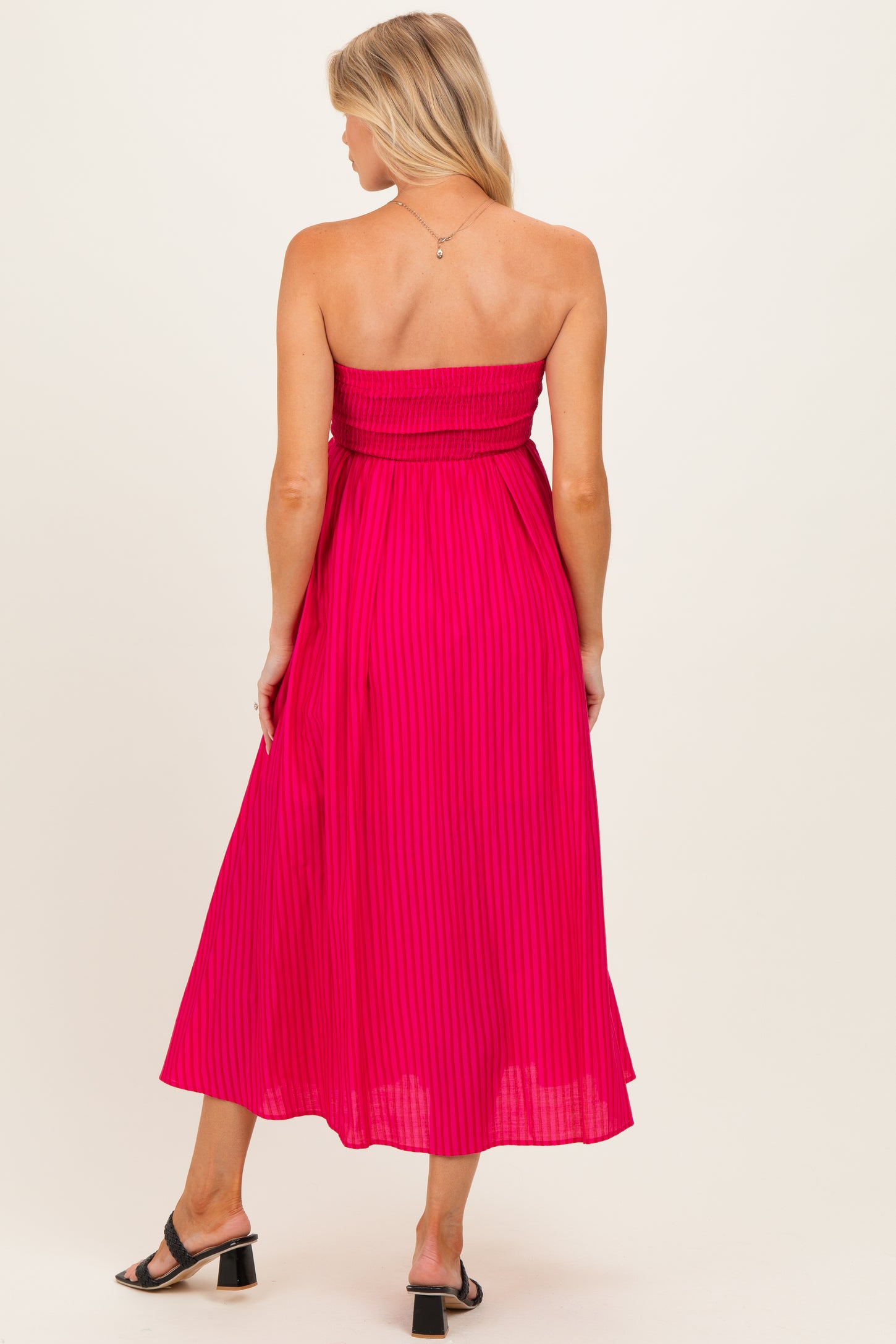 woman wearing a pink strapless maternity dress with a fitted bodice and flowy skirt, back view