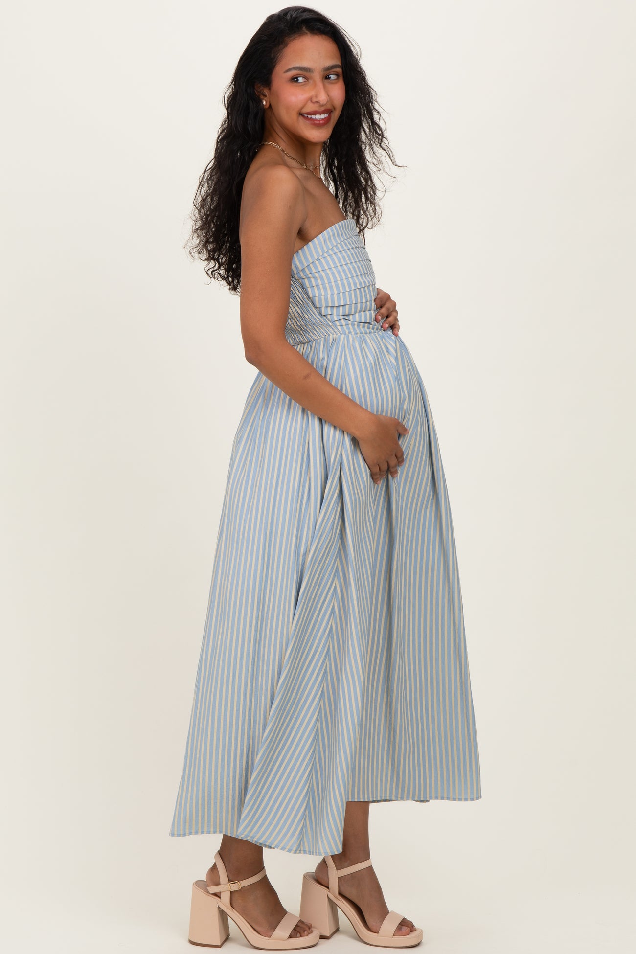 woman wearing a light blue striped maternity maxi dress with a fitted bodice and holding her baby bump