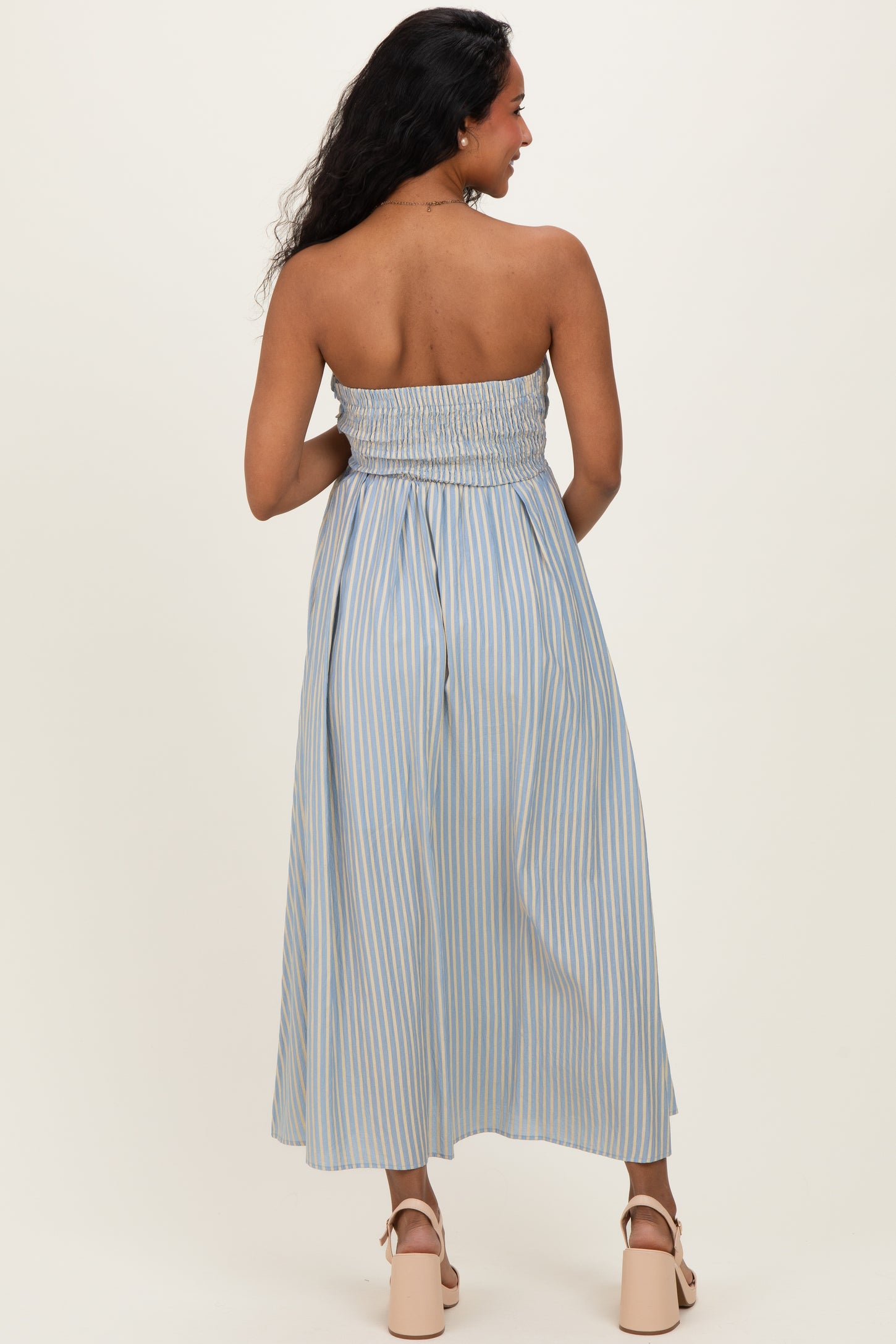 woman wearing a light blue striped strapless maternity dress with a smocked bodice and a flowy skirt, showing a baby bump