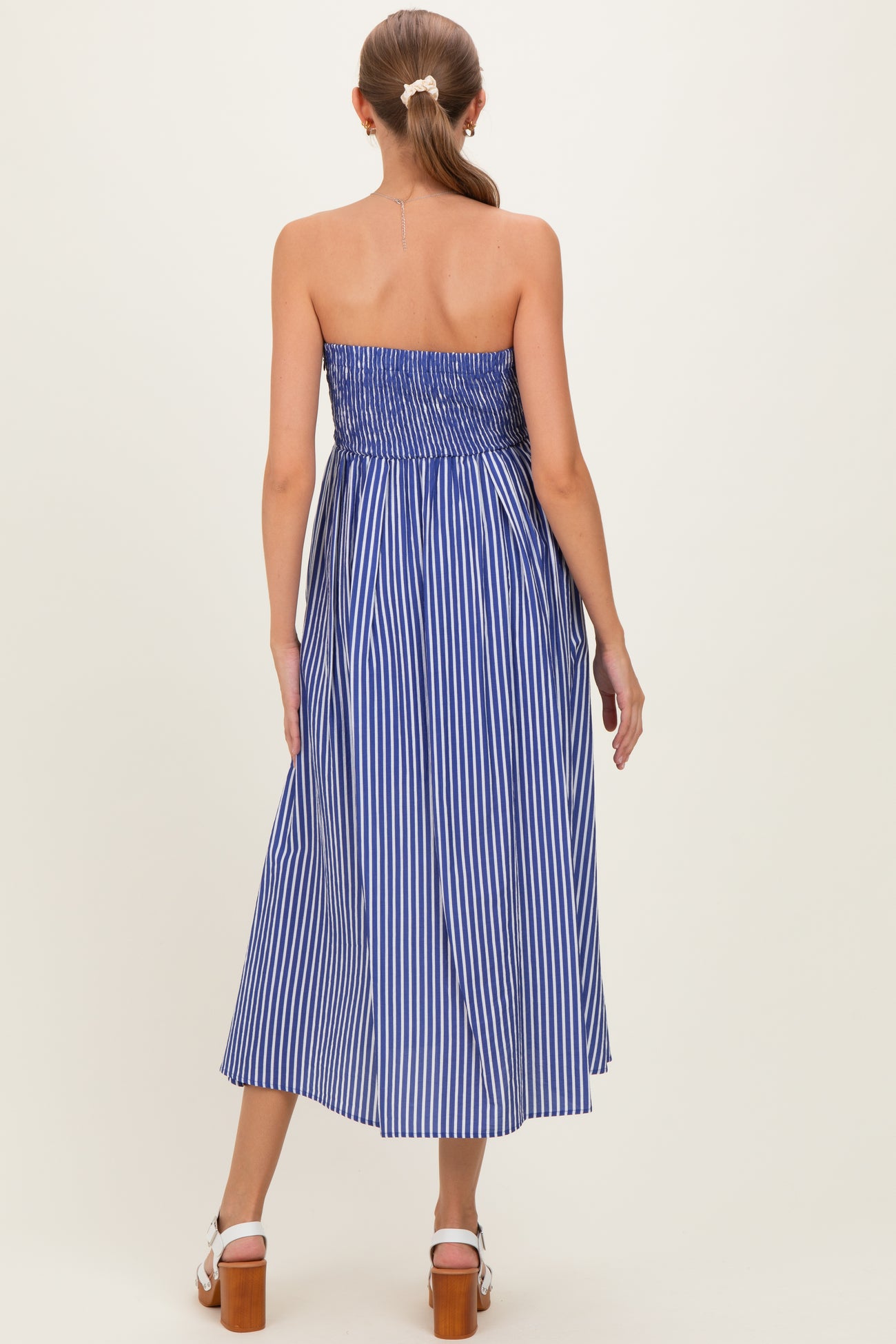 woman wearing a blue and white striped strapless maternity maxi dress, showing a fitted bodice and flowing skirt from the back