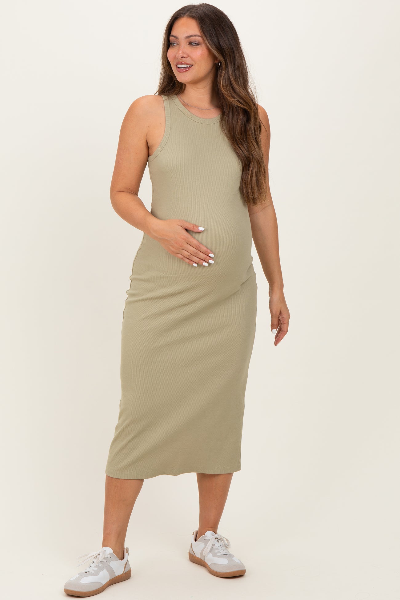 woman wearing a light olive green sleeveless maternity midi dress and holding her baby bump