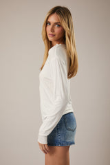 woman wearing a white long sleeve top and denim mini skirt, posed sideways with long hair down