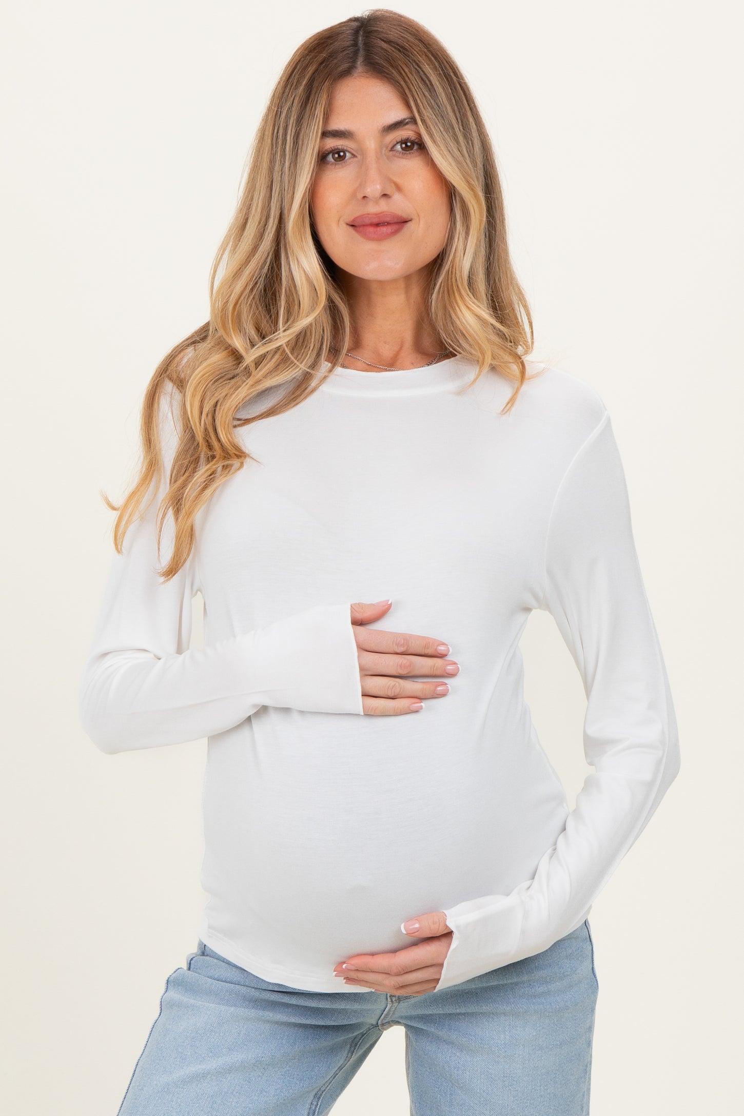 woman wearing a white long sleeve maternity top and holding her baby bump