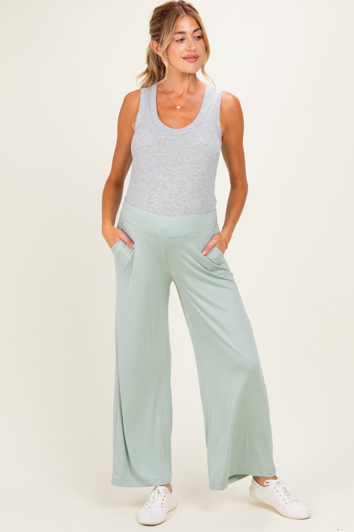 woman wearing a light grey tank top and light green wide-leg maternity pants with pockets and a visible baby bump