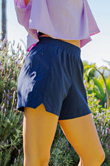 woman wearing navy blue athletic shorts with an elastic waistband and side slits, paired with a light purple top