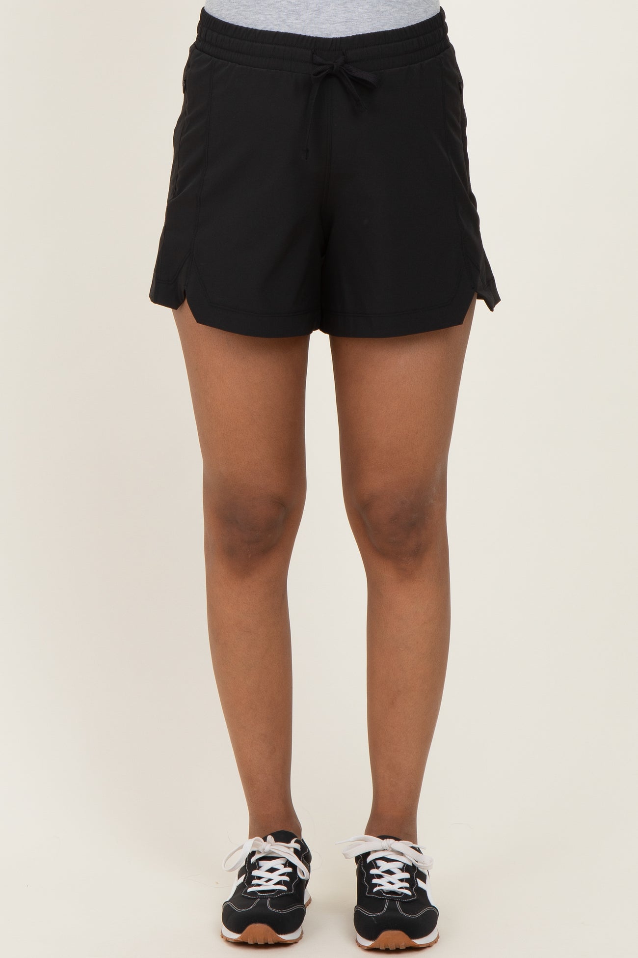 woman wearing black maternity shorts with a drawstring waistband and side slits, styled with athletic shoes