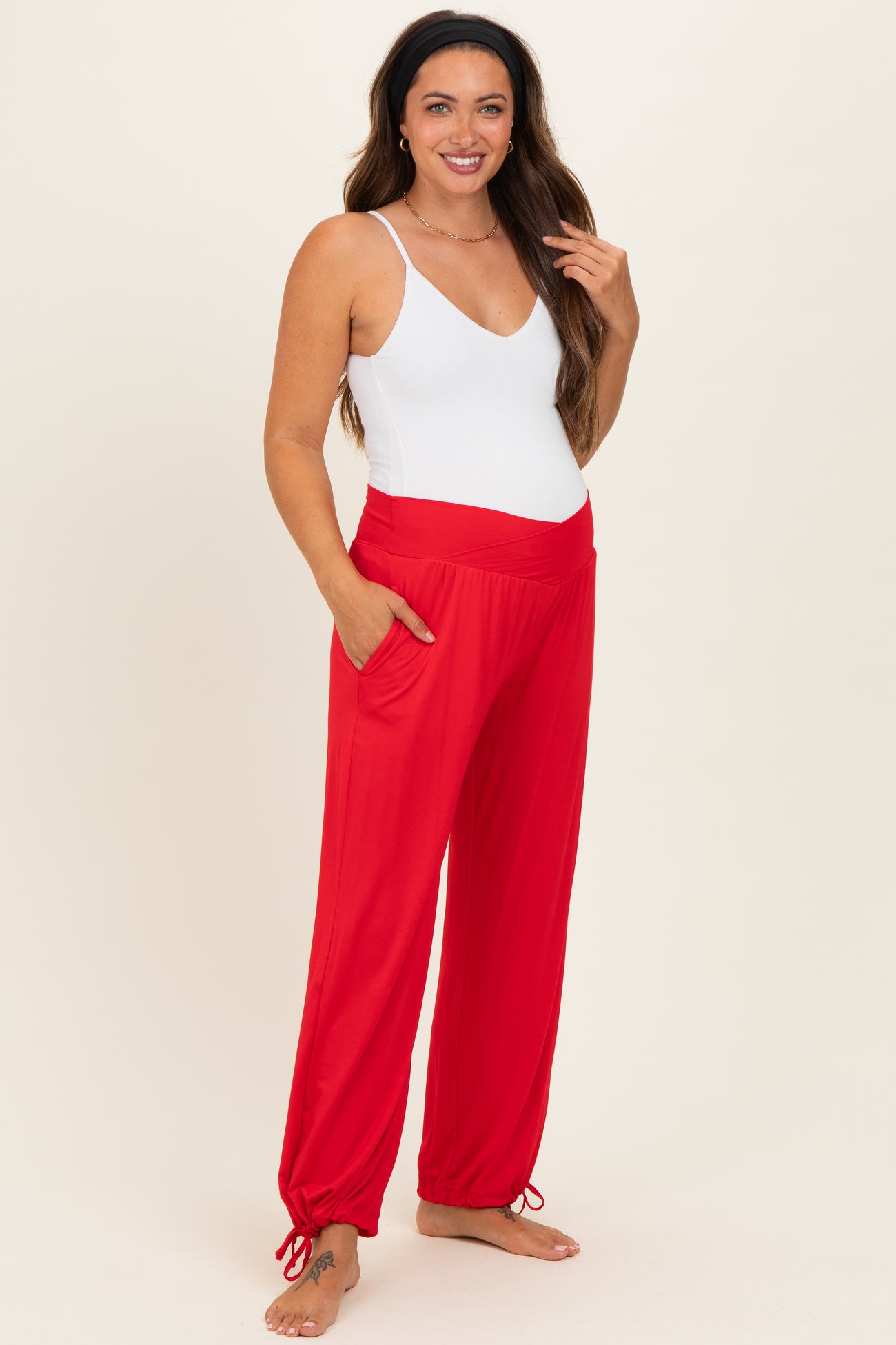 woman wearing a white maternity tank top and red wide-leg maternity pants with pockets, showing her baby bump
