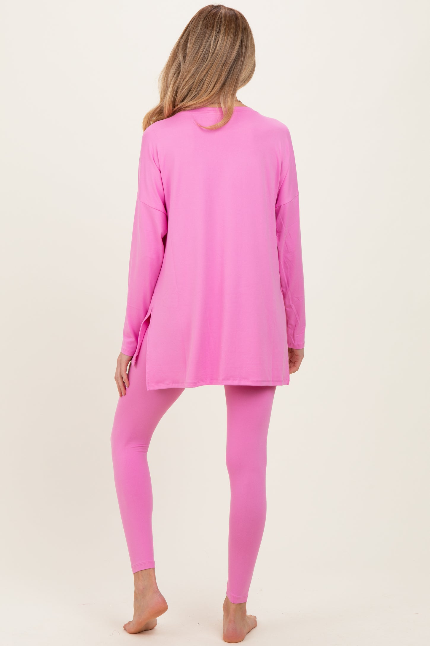 woman wearing a pink maternity top and matching leggings, facing away from the camera, showing a relaxed fit
