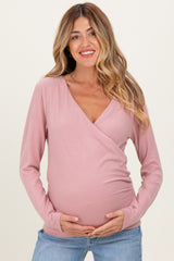 woman wearing a soft pink maternity wrap top and holding her baby bump