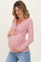 woman wearing a light pink long sleeve maternity top and holding her baby bump