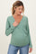 woman wearing a green maternity wrap top and showing her baby bump with a relaxed smile